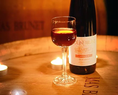 Mise en situation de la Cartagene (Dolinebrune, vin de liqueur) : verre rubis et bouteille posES sur un fut Mas Brunet, bougies allumees, ambiance intime.