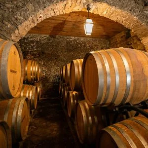 Chai a barriques voute en pierre : alignement de futs de chene sous une lanterne suspendue, ambiance chaleureuse. Tres belle cave (servie en 300x300).