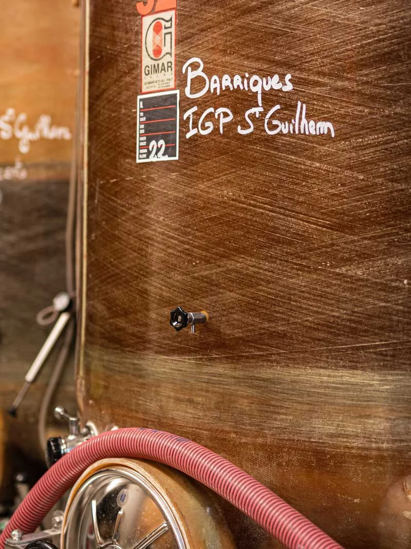Cuve tronconique en bois dans le chai, inscription à la craie 'Barriques IGP St Guilhem 22', vanne et tuyaux. Détail authentique de la cave/vinification.