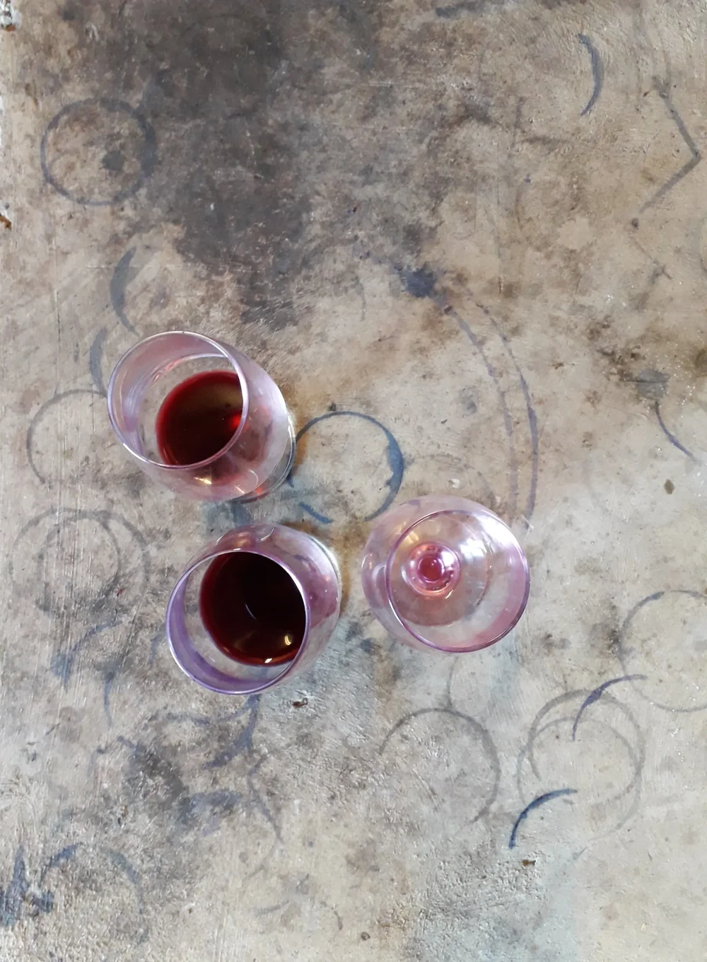 Trois verres de vin rouge vus de dessus, posés sur une dalle de pierre marquée de ronds de verres, lumière douce. Ambiance dégustation conviviale et authentique.