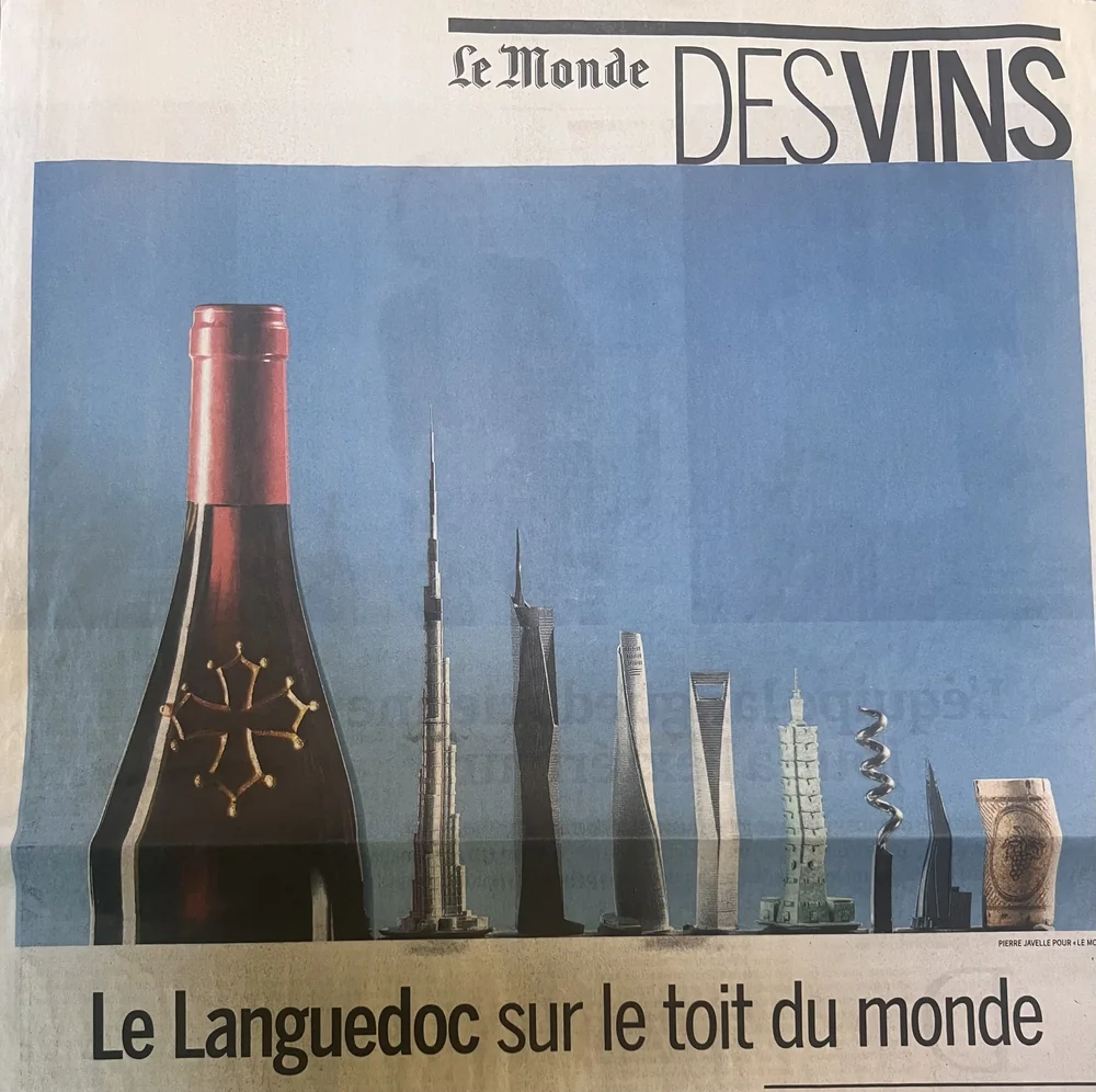 Photo d'une coupure de presse 'Le Monde des Vins' (une de journal, avril 2026) titree 'Le Languedoc sur le toit du monde' avec une bouteille a croix occitane devant des gratte-ciels. Contenu presse/actualite du domaine, pas un visuel propre du domaine ; utile pour une rubrique presse.