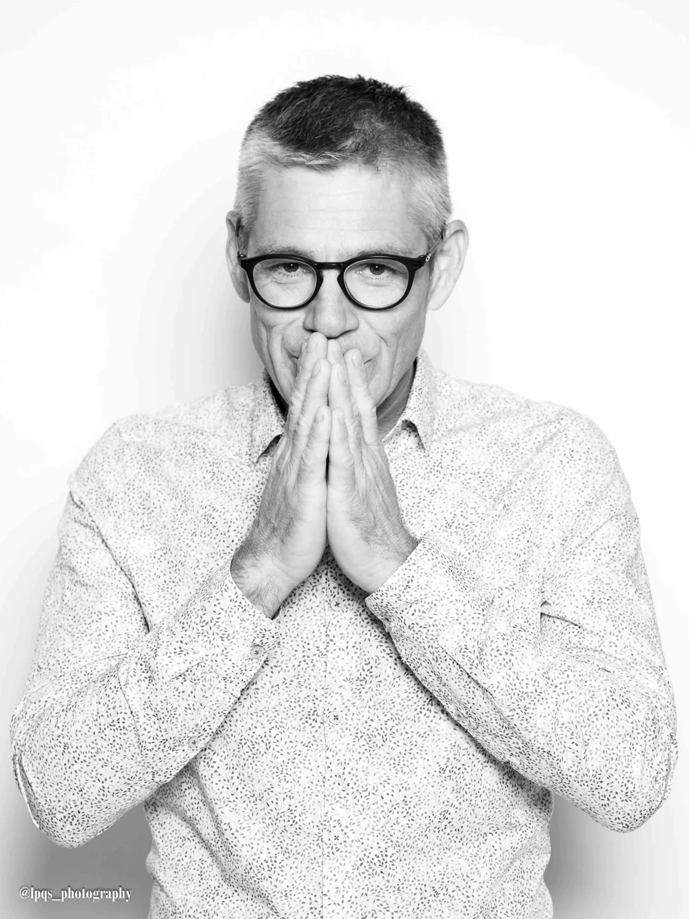 Portrait studio noir et blanc tres soigne de Christophe Puech (lunettes, chemise a motifs, mains jointes devant le visage). Photo professionnelle (credit @lpqs_photography), forte presence, ideale pour une page 'le vigneron' ou edito.
