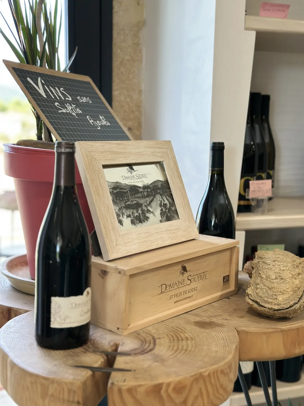 Mise en scene de la marque Domaine Souyris : coffret bois grave 'DOMAINE SOUYRIS - St Felix de Lodez' contenant un cadre avec une illustration noir et blanc du mas/domaine et de ses vignes (avec le logo amphore-grappe), bouteille Souyris a cote et ardoise 'Vins sans sulfites ajoutes'. Photo prise au
