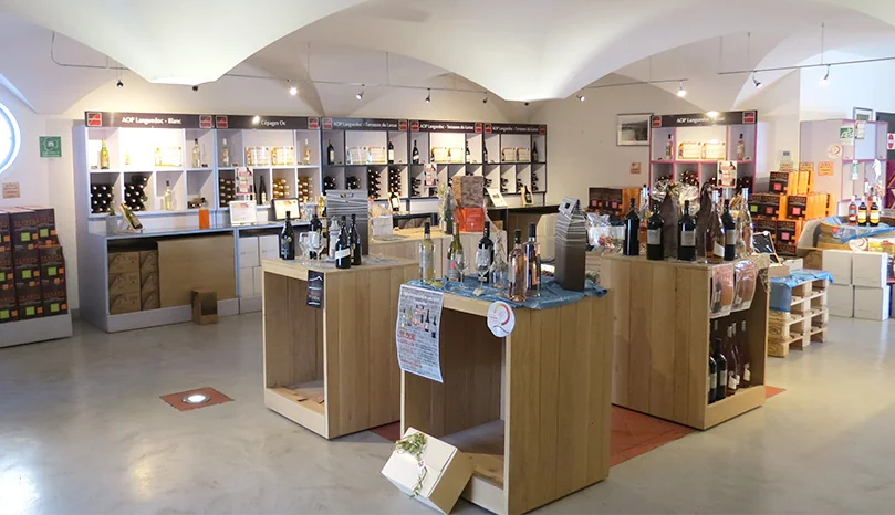 Interieur de la boutique / caveau Fonjoya : salle voutee en pierre, presentoirs en bois clair, bouteilles classees par appellation. Met en valeur l'espace de degustation et de vente.