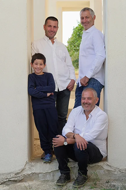 Portrait familial vertical : les trois freres Ravaille (vignerons) et un enfant, poses dans l'encadrement d'une porte en pierre claire. Tres beau portrait, lumiere douce, fort capital sympathie/transmission.