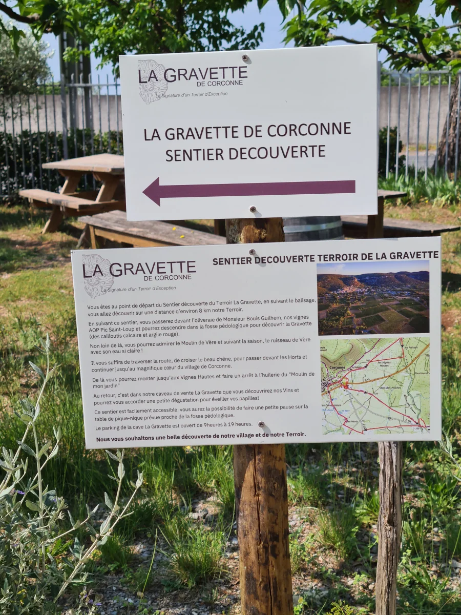 Panneaux du 'Sentier Decouverte Terroir de la Gravette' (panneau directionnel + panneau explicatif avec carte) dans la garrigue. Faible valeur photographique mais appartient au domaine et porte le logo.