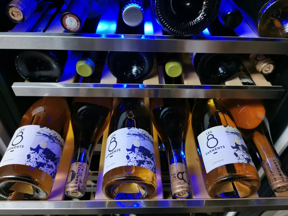 Bouteilles Les 8 Sarments couchées dans une cave/armoire à vin éclairée en bleu. Ambiance cave de garde.