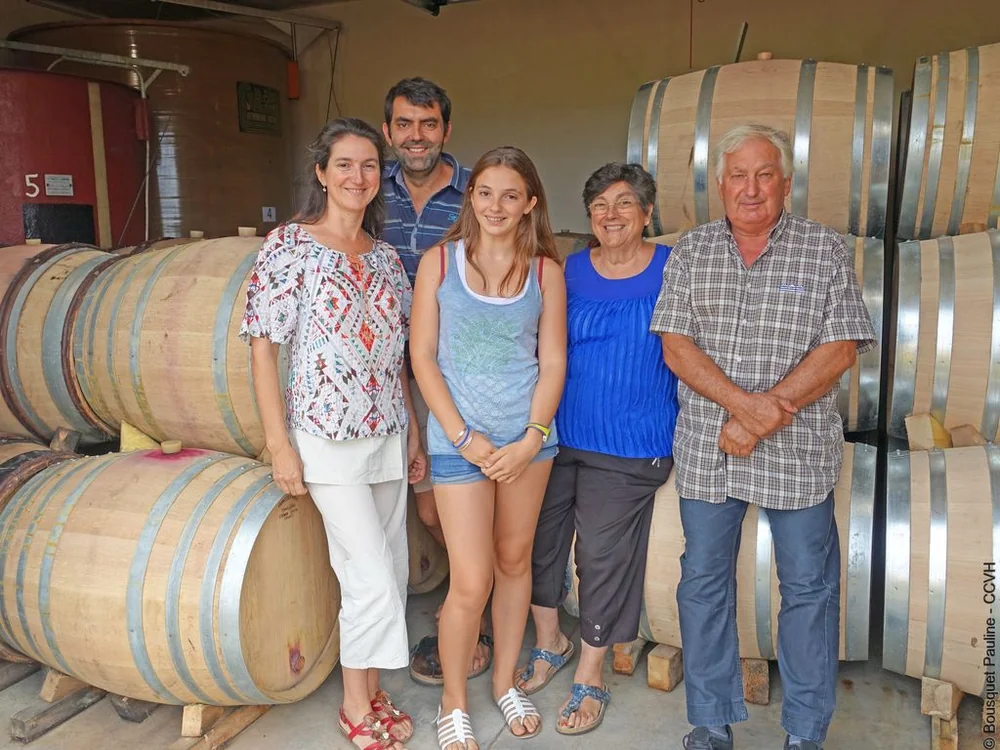 Portrait de la famille Visseq (cinq personnes, trois generations) posant dans le chai devant les barriques de chene et les cuves. Photo lumineuse, conviviale, parfaite pour incarner le domaine et creer la confiance. 1024x768, credit Pauline Bousquet - CCVH (via Herault Tourisme).