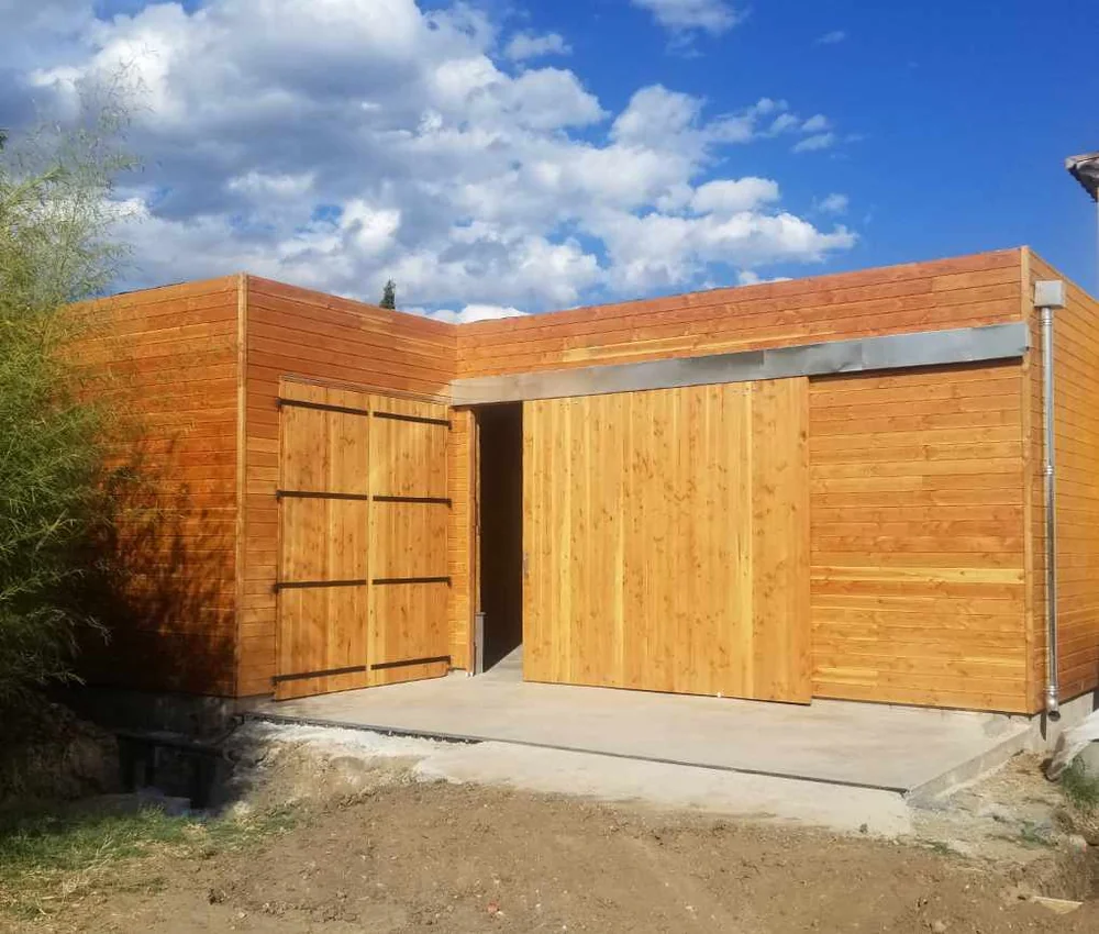 Le nouveau chai en bois (construit en 2020) vu de l'exterieur, bardage clair et grande porte coulissante sous ciel bleu. Architecture du domaine.