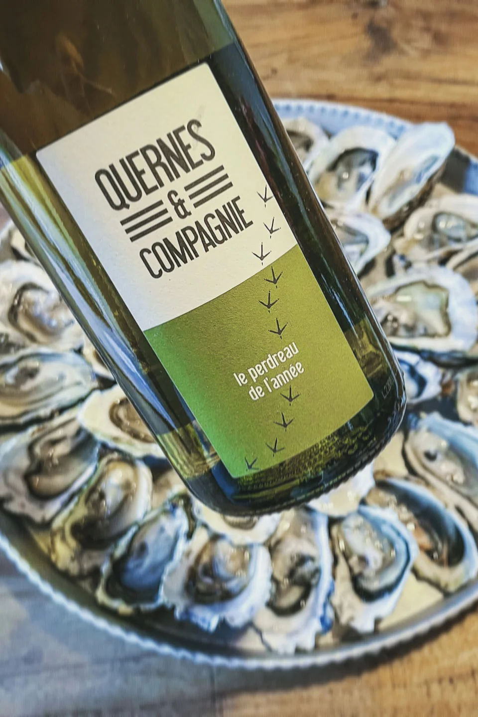 Bouteille Quernes & Compagnie 'Le Perdreau de l'annee' posee sur un plateau d'huitres fraiches. Mise en situation gourmande.